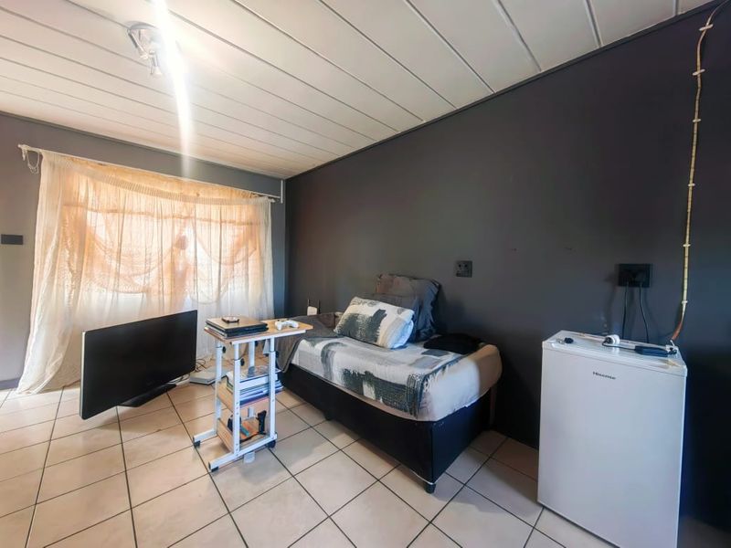 A bedroom featuring tiled flooring, dark accent wall, and a panelled ceiling, providing a functional living space.