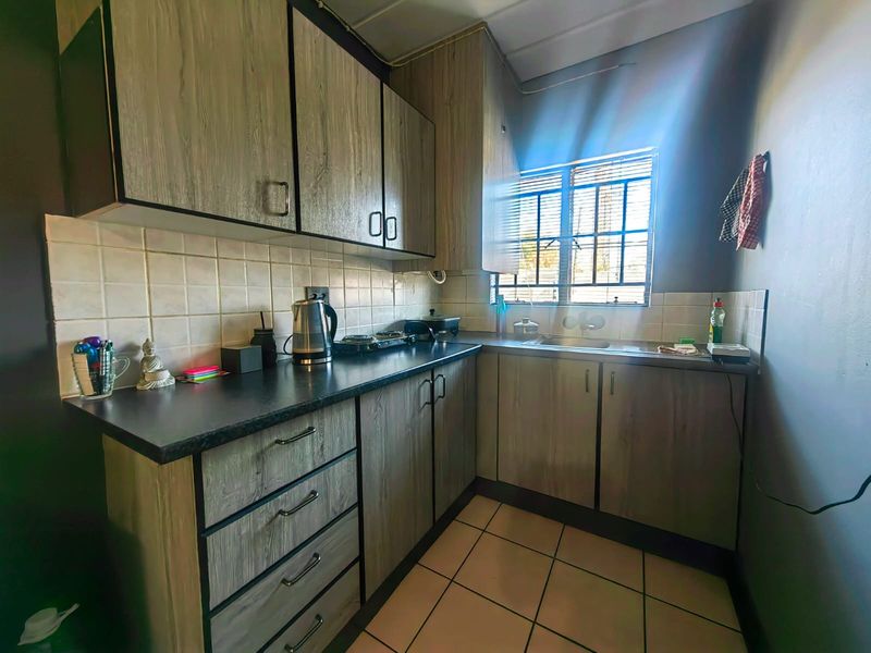 Compact kitchen featuring wood-grain cabinetry, dark laminate countertops, tiled backsplash, and a stainless steel sink with natural light from the window.