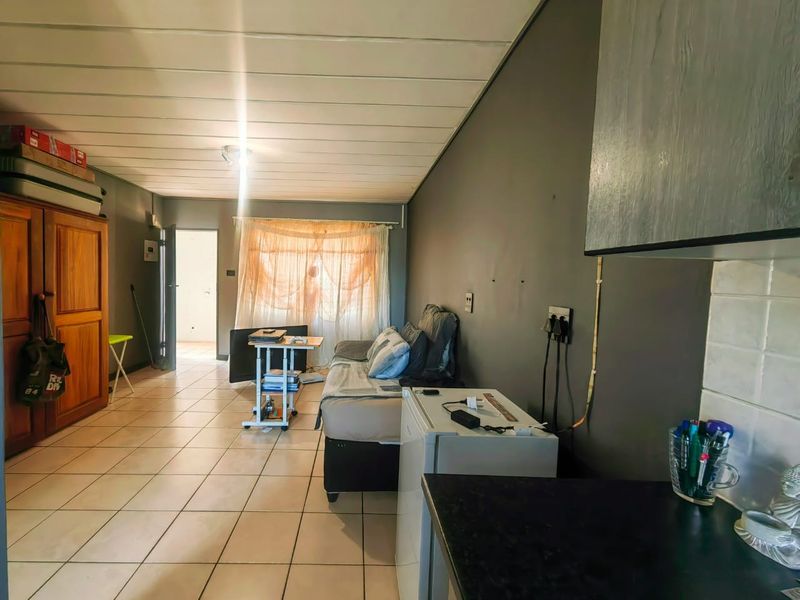 Open-plan living area featuring tiled flooring, a compact kitchen corner, and direct access to an exterior entrance.