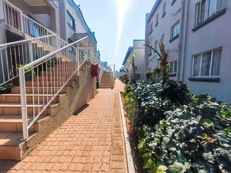 Exterior view of an apartment complex featuring paved walkways, external staircases with metal railings, and landscaped garden beds between the building blocks.