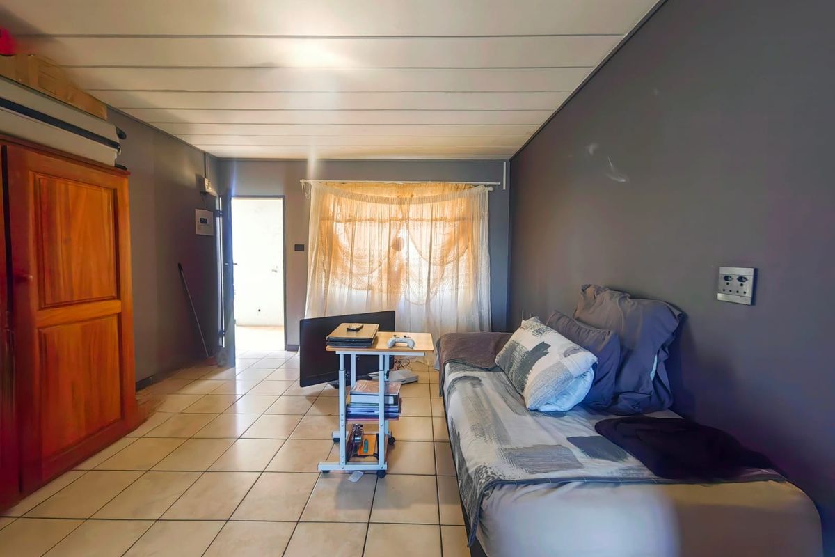 A bedroom featuring tiled flooring, dark grey walls, and a panelled ceiling, with direct access to an adjacent outdoor area.