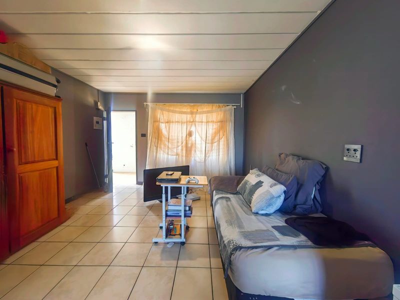 A bedroom featuring tiled flooring, dark grey walls, and a panelled ceiling, with direct access to an adjacent outdoor area.