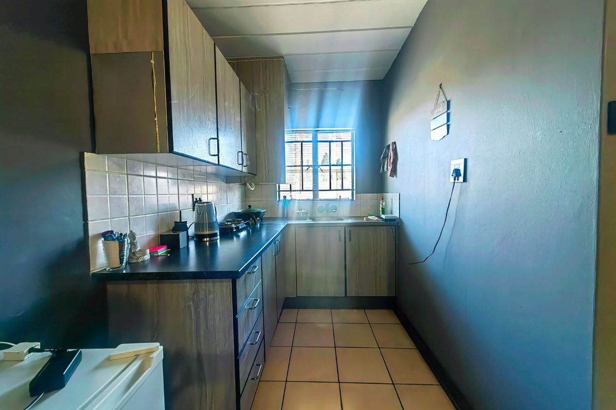 A compact galley-style kitchen featuring wood-look cabinetry, dark laminate countertops, tiled flooring, and a window providing natural light.