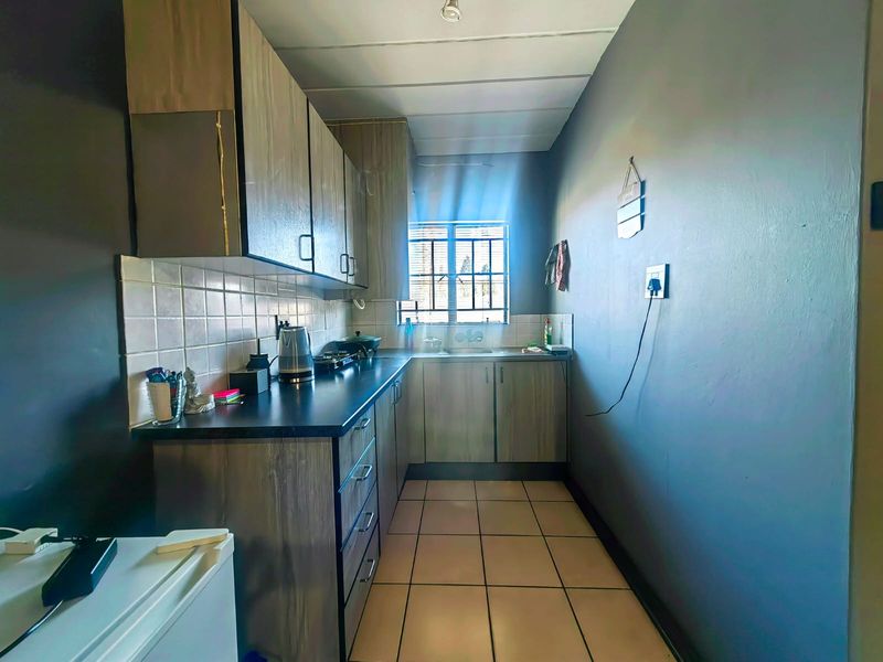 A compact galley-style kitchen featuring wood-look cabinetry, dark laminate countertops, tiled flooring, and a window providing natural light.