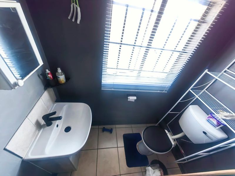 A compact bathroom featuring a wall-mounted basin with a modern black faucet, a standard toilet, and a window with fitted blinds.