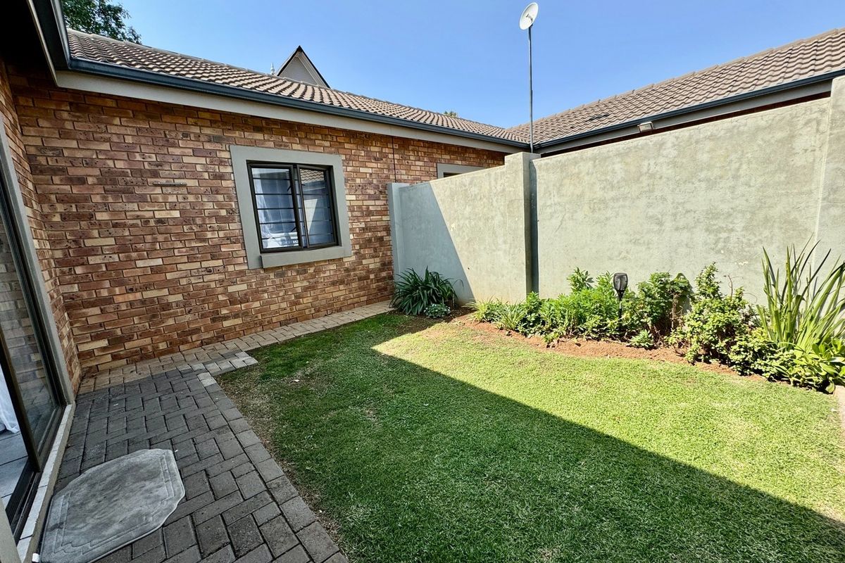 A private rear courtyard featuring a paved patio area, a small lawn, and a perimeter boundary wall.