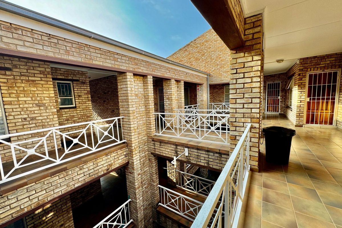 Exterior view of an apartment complex featuring multi-level walkways with brick facades, tiled flooring, and white metal railings.