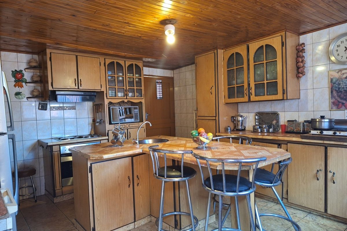 A dated kitchen featuring wood cabinetry, tiled backsplash, a central island with breakfast bar seating, and a wood-paneled ceiling.