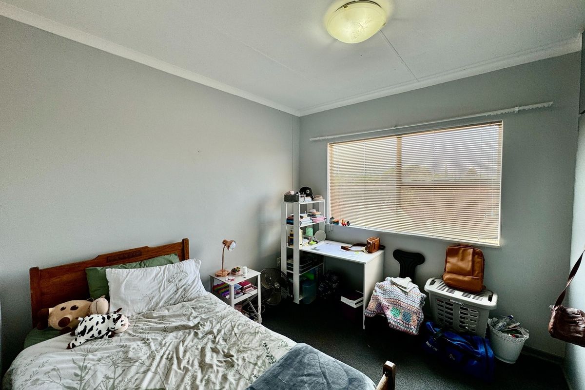 A functional bedroom featuring a large window with fitted blinds, neutral wall finishes, and a central ceiling light fixture.