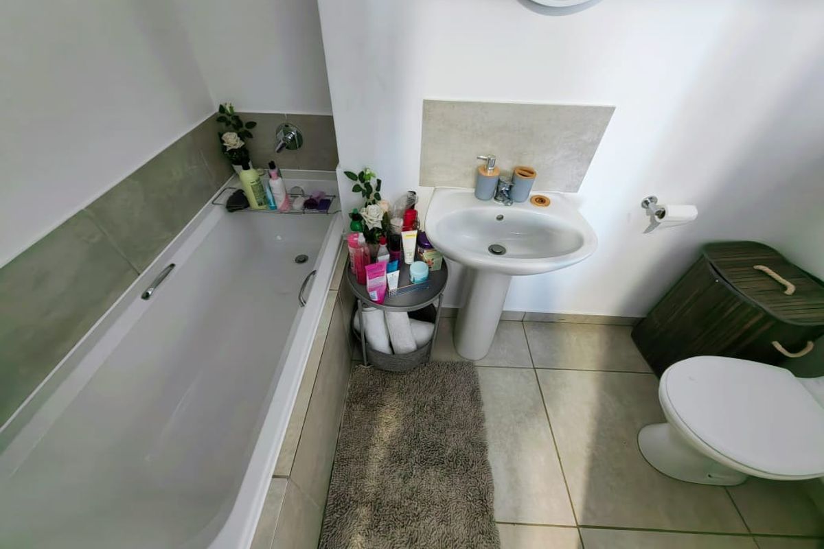 A functional bathroom featuring a standard bathtub, pedestal basin, and toilet with neutral wall and floor tiling.