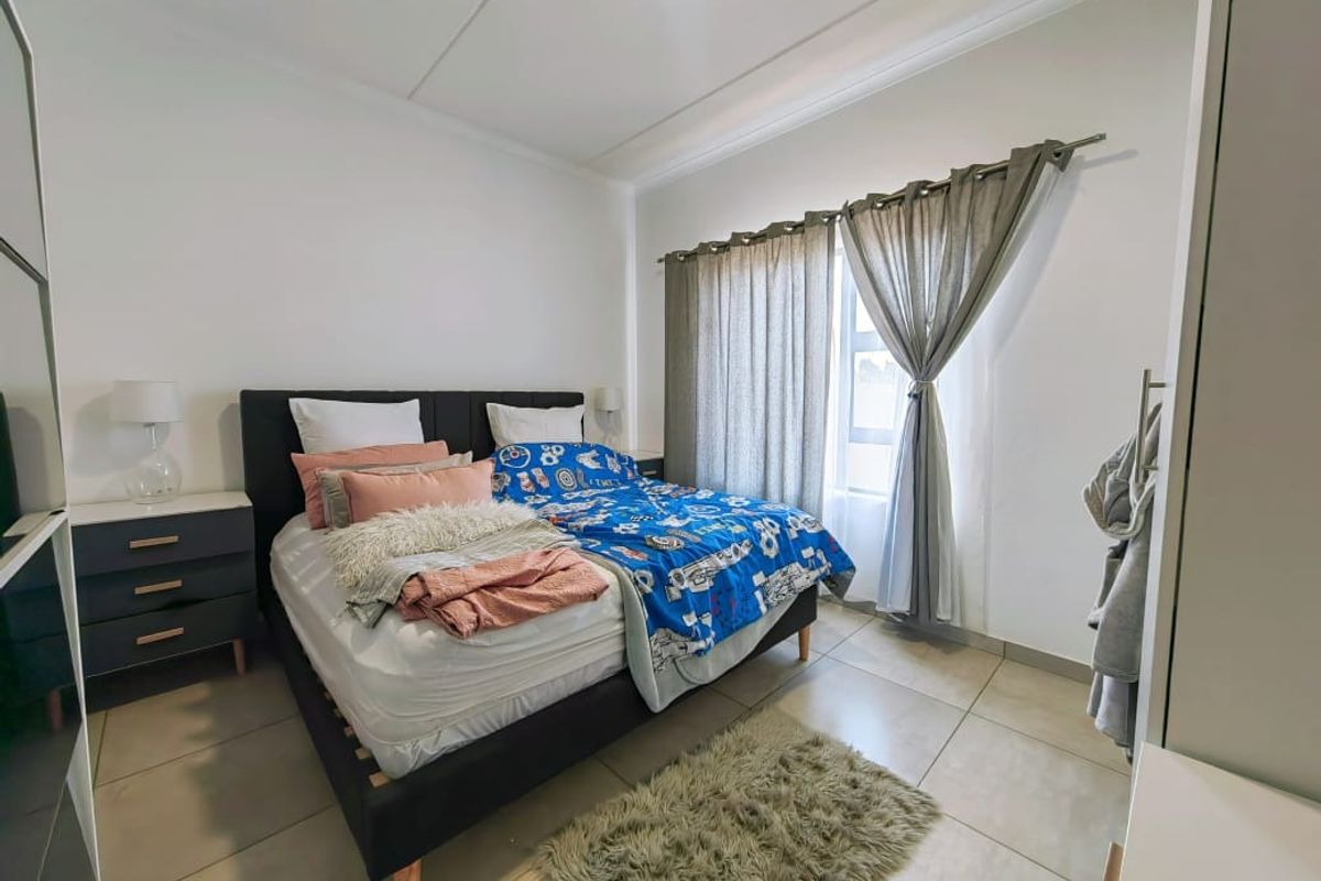 A well-lit bedroom featuring neutral floor tiles, built-in wardrobe space, and a window with curtain tracks.