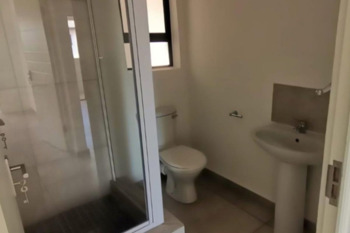 A clean, modern bathroom featuring a glass-enclosed shower, pedestal basin, and toilet with neutral floor tiling.