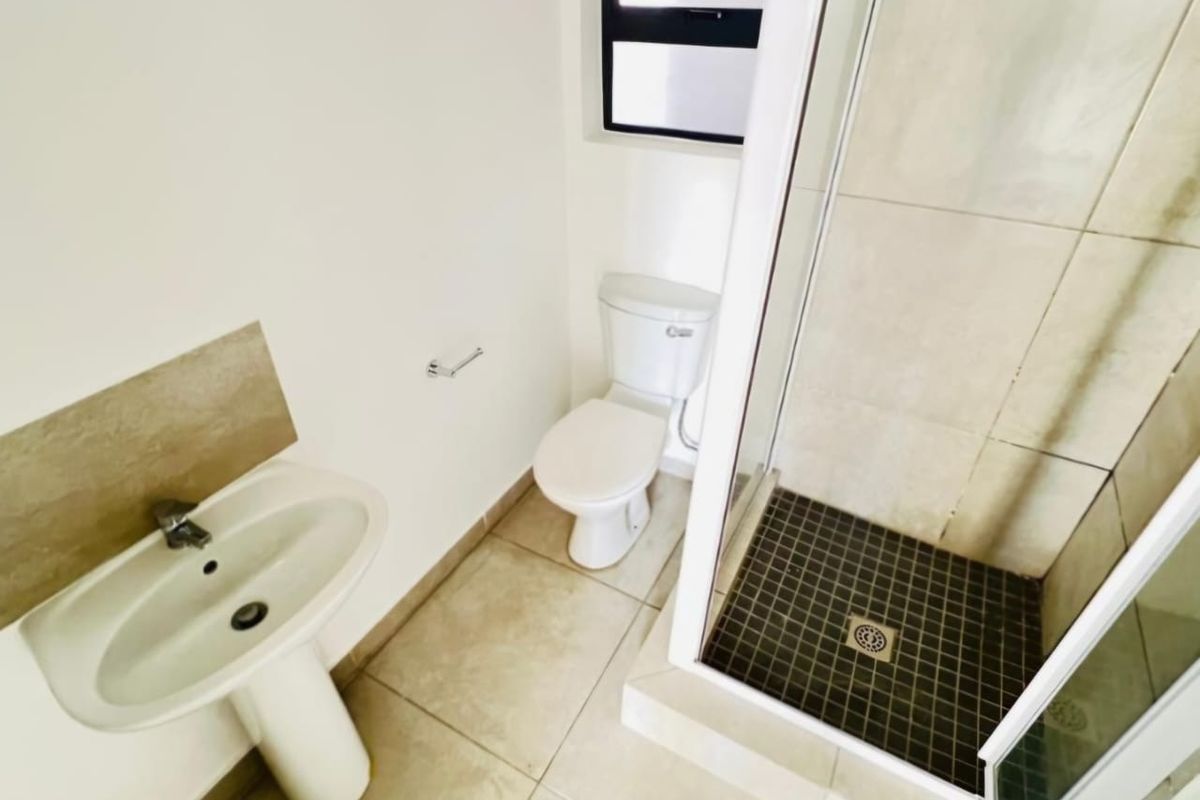 A clean and functional bathroom featuring a pedestal basin, a white toilet, and a glass-enclosed shower with tiled flooring.
