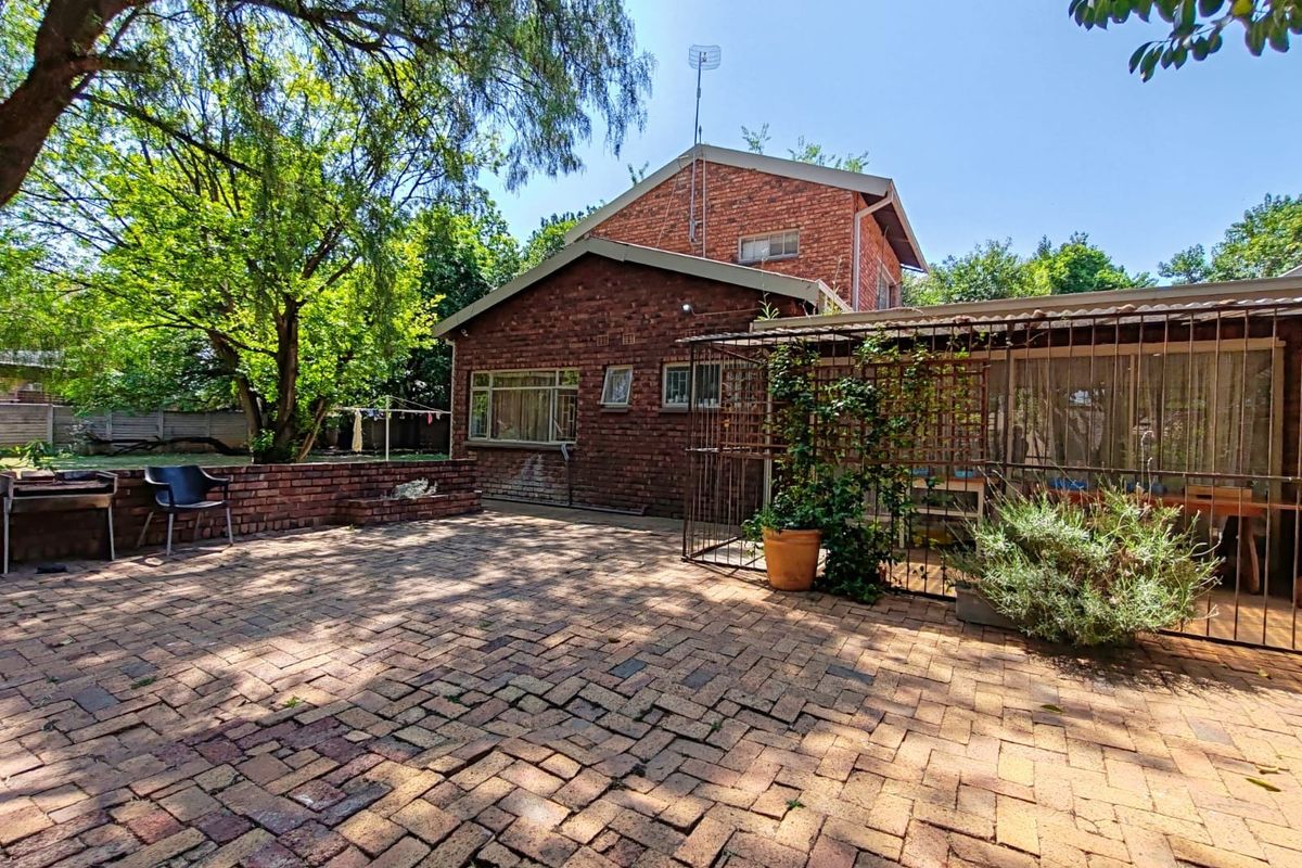 Rear exterior view of the property featuring a brick-paved patio area, established garden, and a covered outdoor space with security gate.
