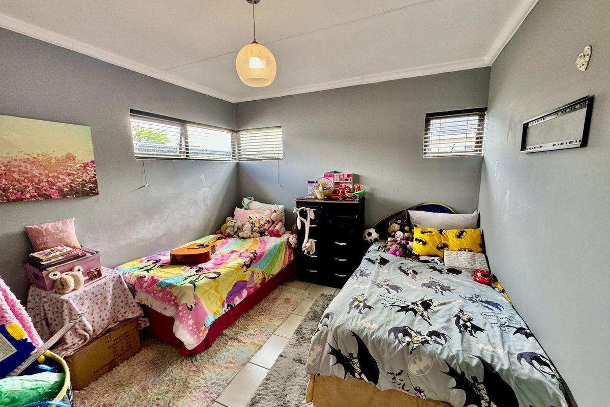 A functional bedroom featuring tiled flooring, neutral grey walls, and horizontal window blinds, providing a comfortable space for rest.