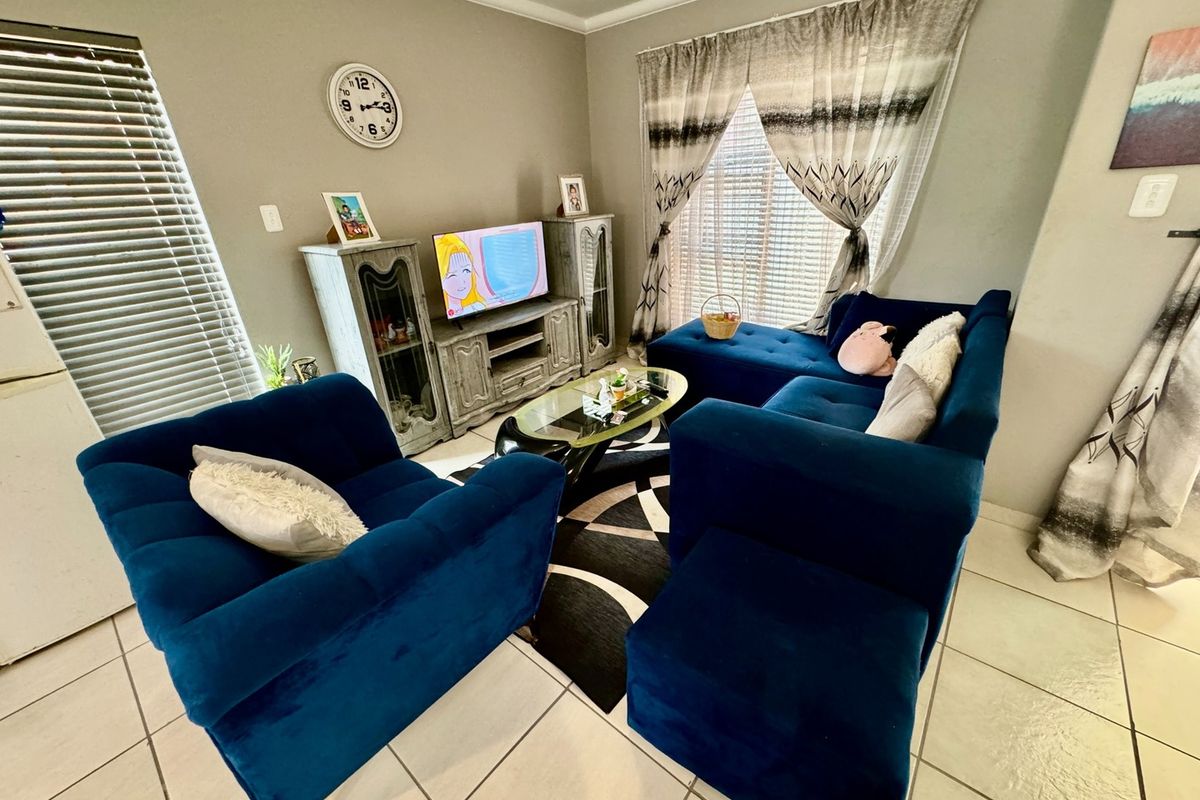 A comfortable living room featuring tiled flooring, neutral wall tones, and large windows with fitted blinds and curtains.