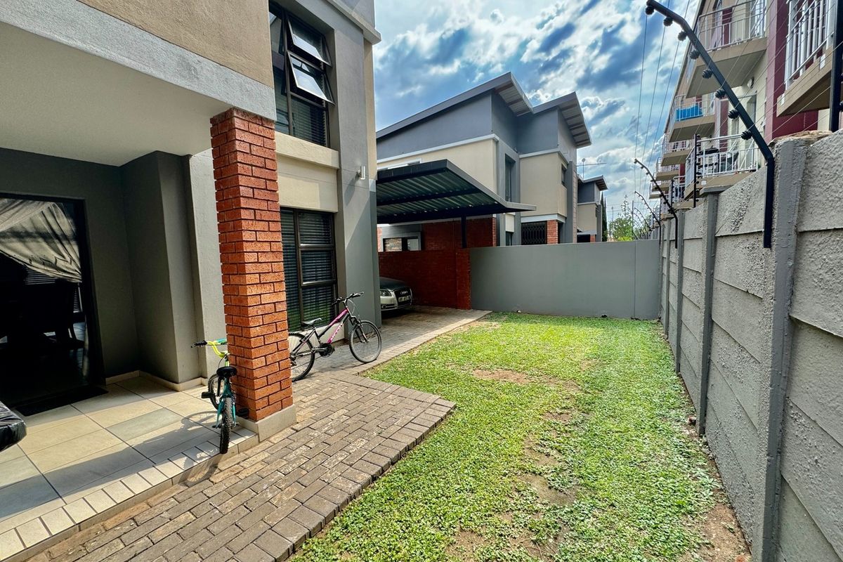 A private rear garden area featuring a paved patio, lawn, and a covered carport structure attached to the townhouse.