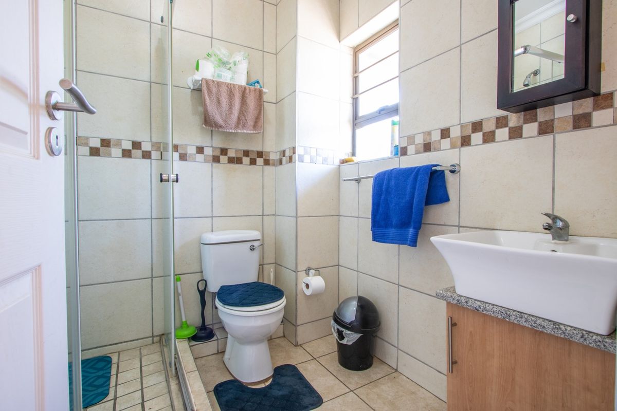 A compact bathroom featuring a glass-enclosed shower, a modern vessel sink with a vanity cabinet, and neutral wall tiling with a decorative border.