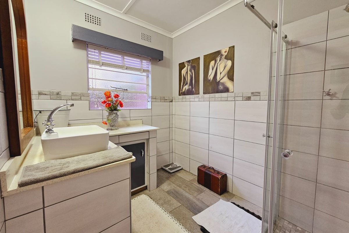 A functional bathroom featuring a glass-enclosed shower, a modern vessel sink vanity, and neutral wall tiling.