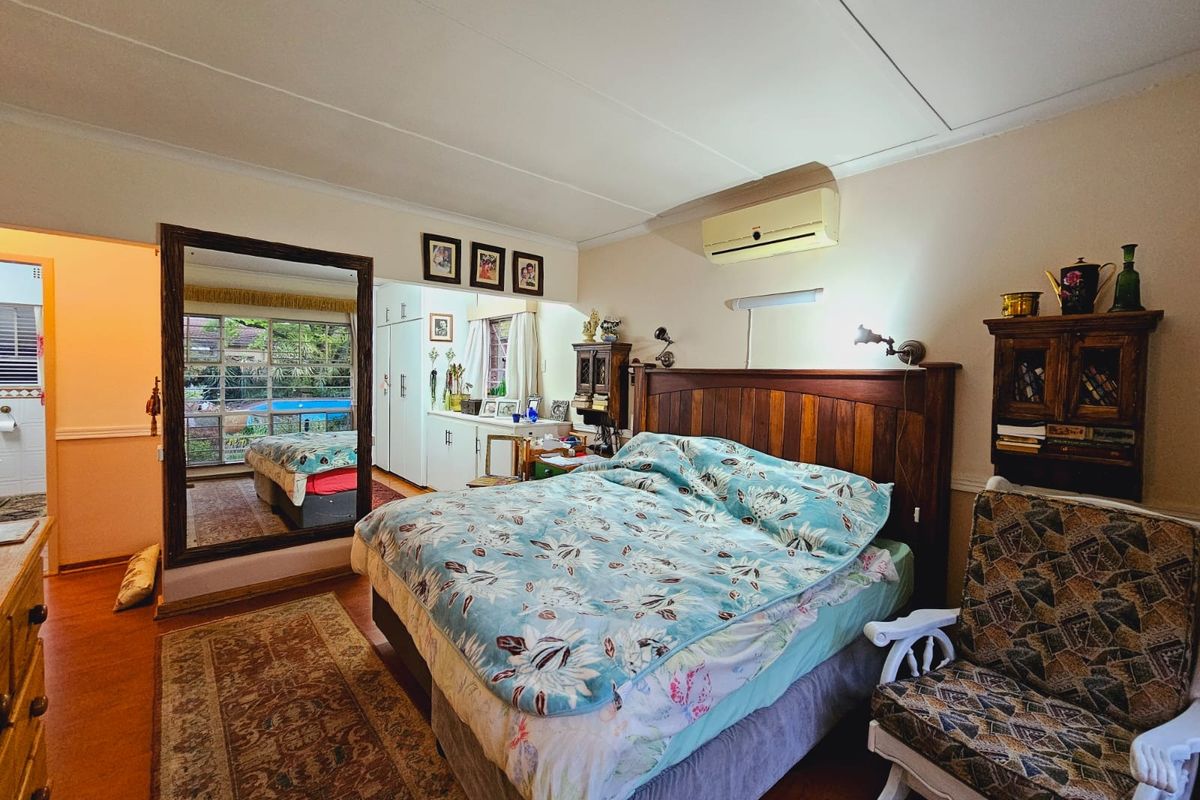 A spacious bedroom featuring a wall-mounted air conditioning unit, built-in cabinetry, and a large mirror reflecting the garden view.