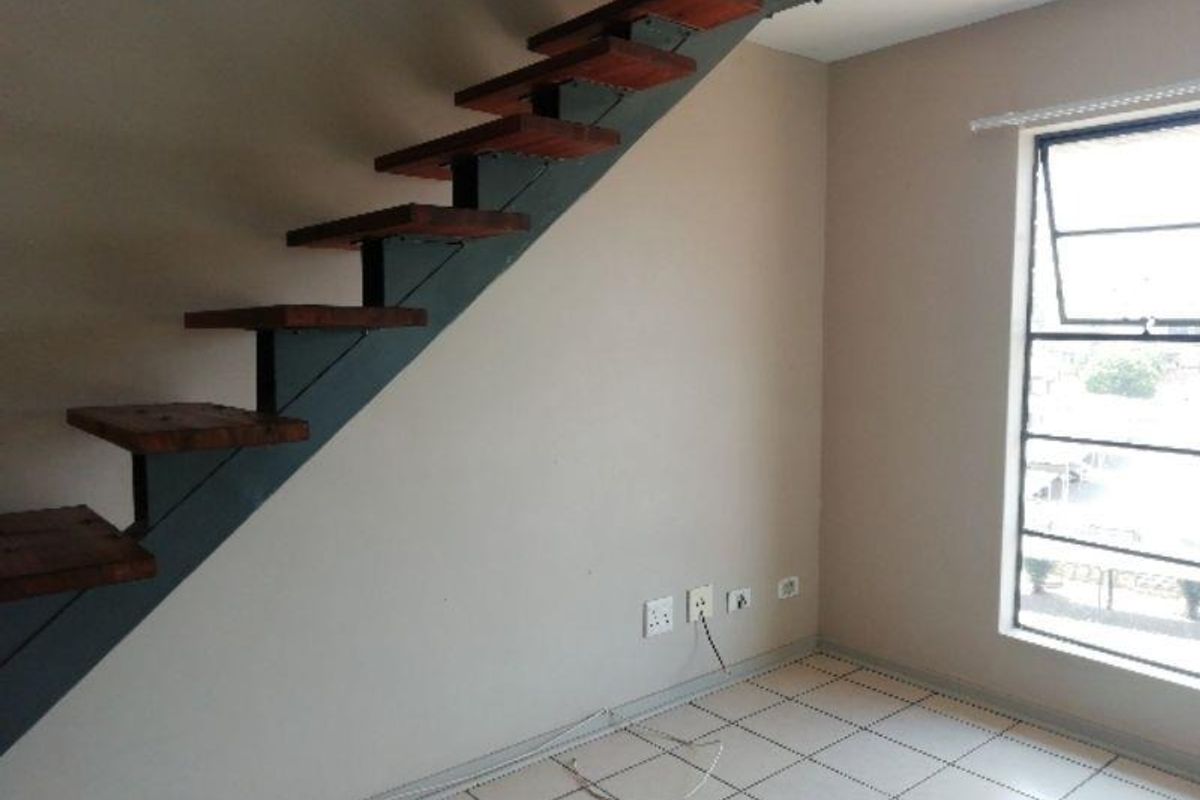 An interior view of a living area featuring a modern floating timber staircase with metal supports, tiled flooring, and a large window.