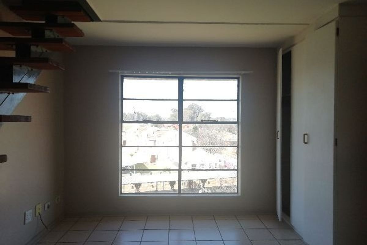 A bedroom featuring tiled flooring, built-in cupboards, and a staircase leading to an upper level, with natural light from a large window.
