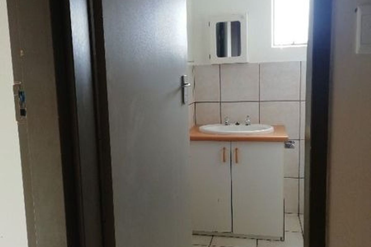 A compact bathroom featuring a vanity unit with a basin, tiled flooring, and wall tiling, viewed through a doorway.