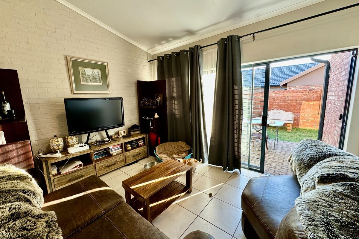 A comfortable living room featuring tiled flooring, a painted brick feature wall, and large sliding glass doors providing direct access to the rear patio.