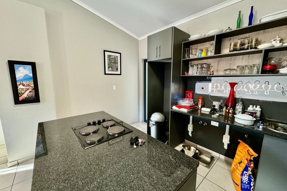 A functional kitchen area featuring a central island with a built-in electric hob, dark cabinetry, and open shelving for storage.