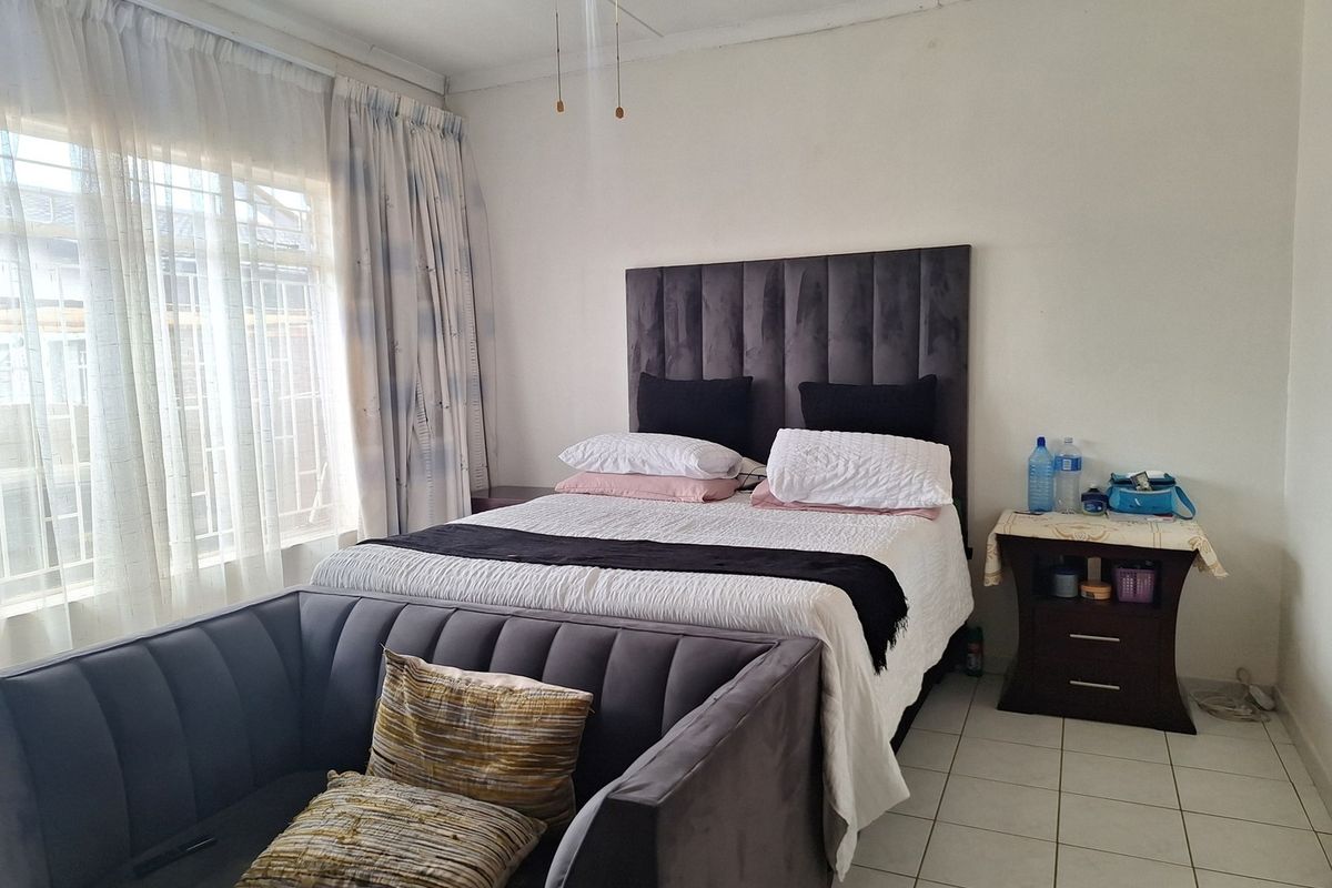 A bedroom featuring tiled flooring, a ceiling fan, and a large window with security bars, providing natural light.