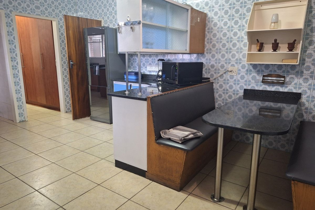 A functional kitchen featuring built-in cabinetry, granite countertops, and a built-in breakfast nook, finished with traditional ceramic wall and floor tiles.