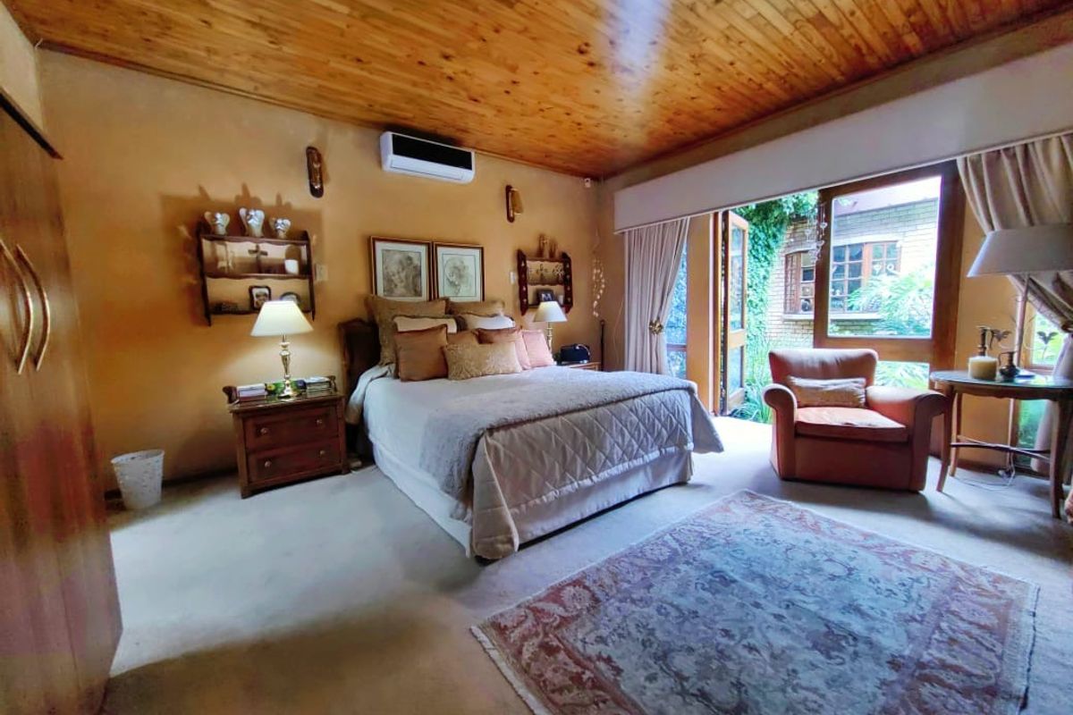 Spacious bedroom featuring a timber-clad ceiling, wall-mounted air conditioning unit, and large glass doors providing direct access to the garden area.