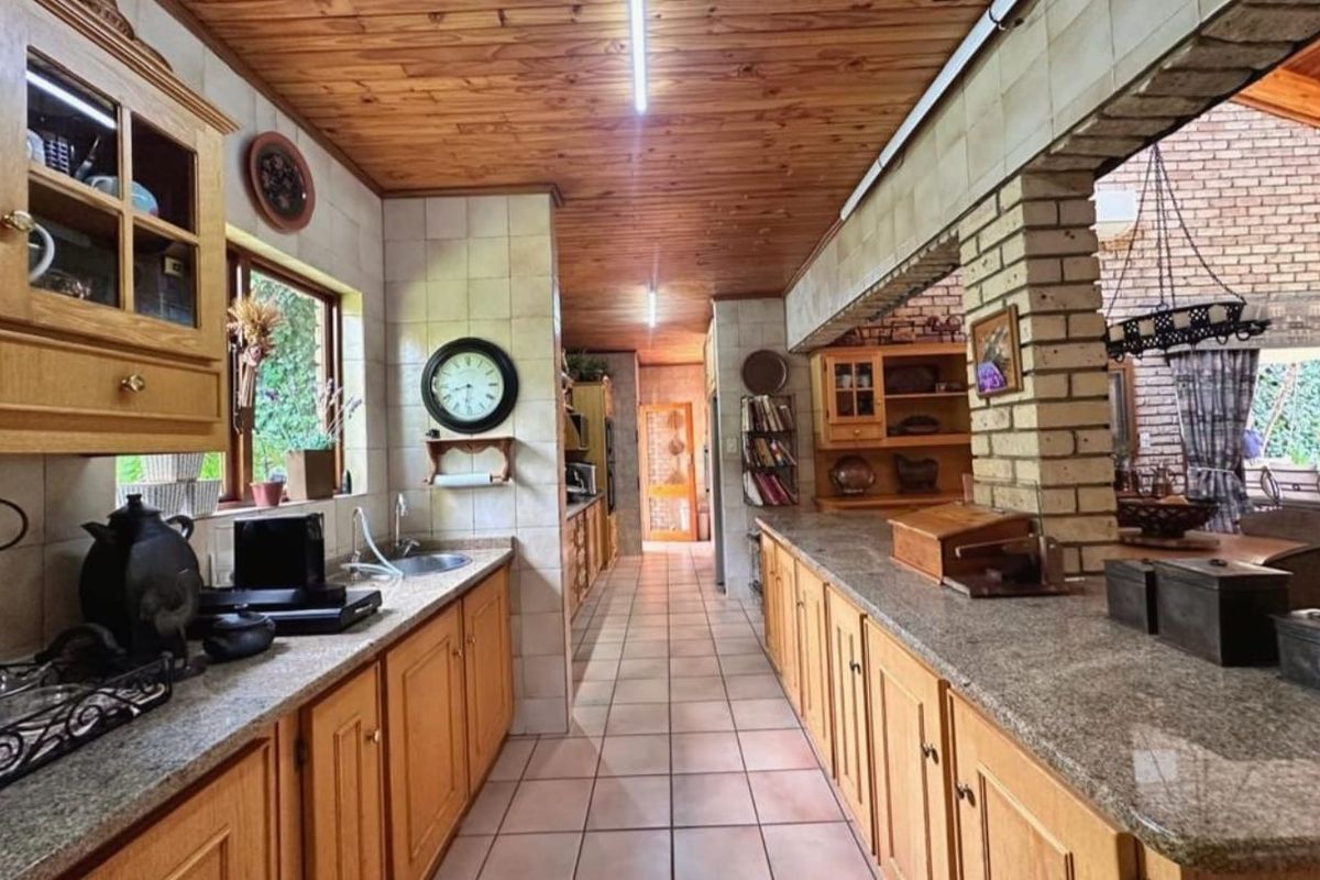 Spacious kitchen featuring extensive wooden cabinetry, granite countertops, tiled flooring, and a distinctive timber-paneled ceiling, offering a traditional aesthetic with ample storage space.