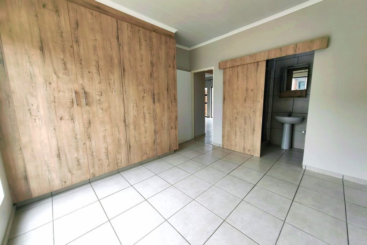 Spacious bedroom featuring built-in wood-finish cupboards, tiled flooring, and an en-suite bathroom accessed via a sliding barn-style door.