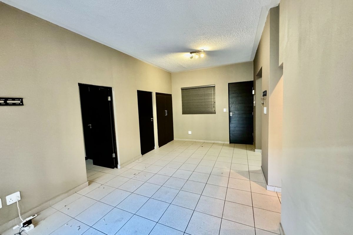 An empty living area featuring tiled flooring, multiple dark-toned interior doors, and a window with fitted blinds.