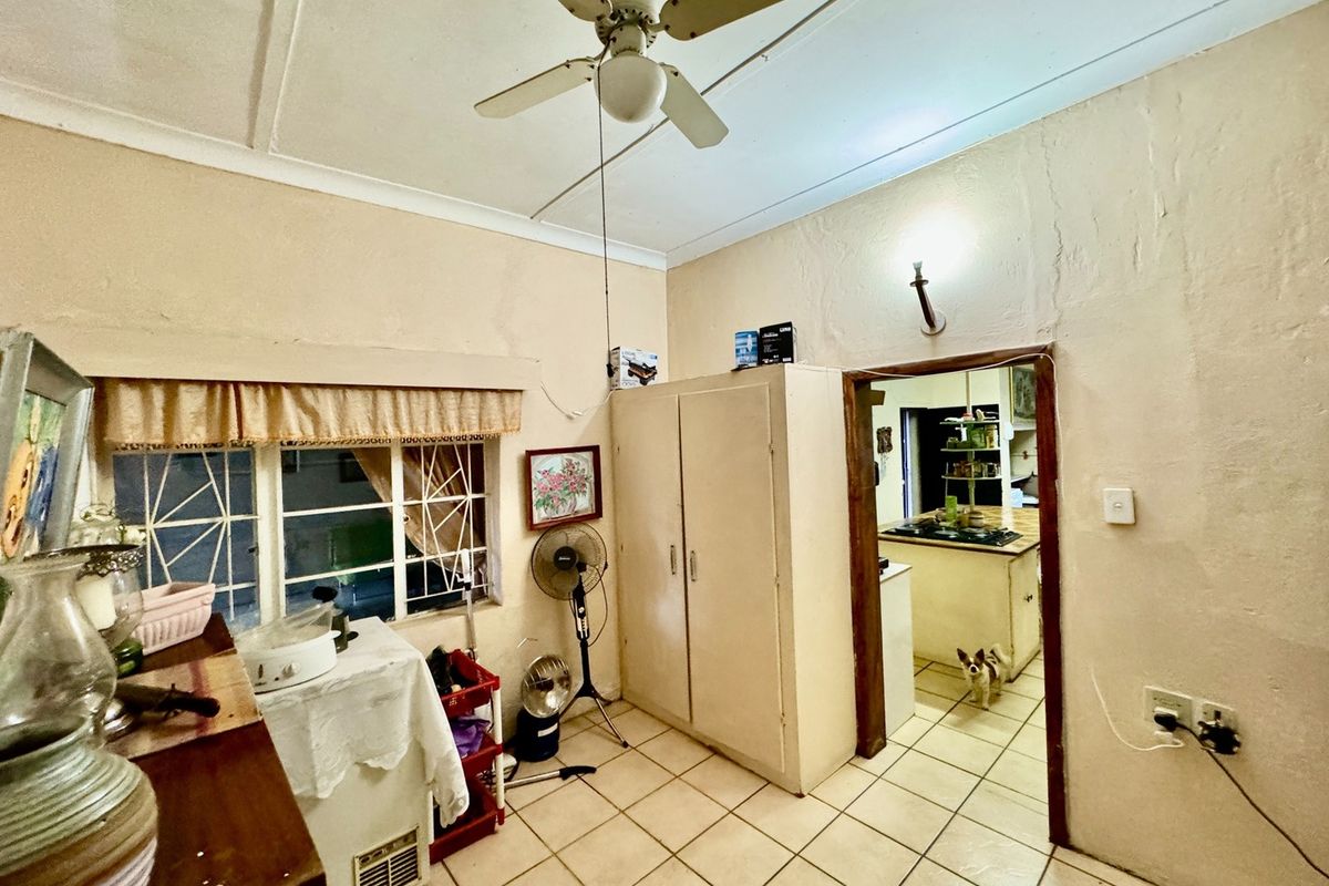 A functional interior space featuring tiled flooring, a ceiling fan, and built-in cabinetry, with a doorway leading through to the kitchen area.
