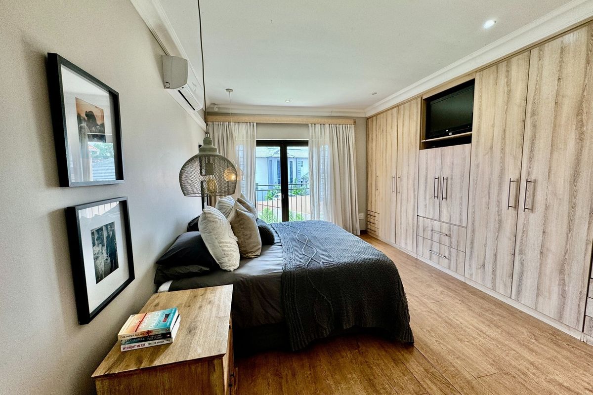 Spacious bedroom featuring extensive built-in wooden cabinetry, wood-look flooring, recessed lighting, and direct access to a private balcony through glass doors.