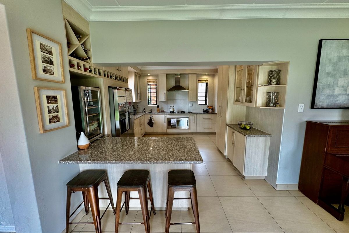 Modern open-plan kitchen featuring light wood cabinetry, granite countertops, a breakfast bar, and integrated stainless steel appliances.