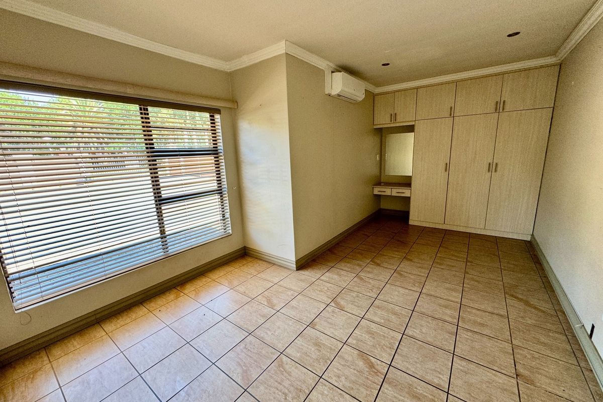 A spacious bedroom featuring built-in cabinetry with a vanity area, tiled flooring, and a wall-mounted air conditioning unit.