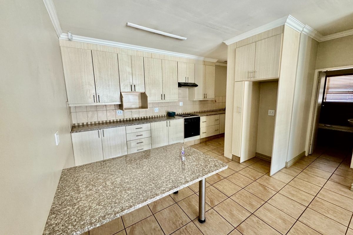 A functional kitchen featuring light wood-grain cabinetry, granite-look countertops, a built-in oven with extractor fan, and tiled flooring throughout.