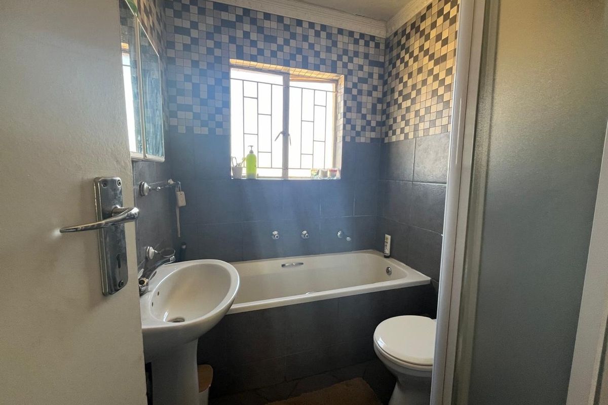 A compact bathroom featuring a bathtub, pedestal basin, and toilet, finished with a combination of dark and checkered wall tiles.