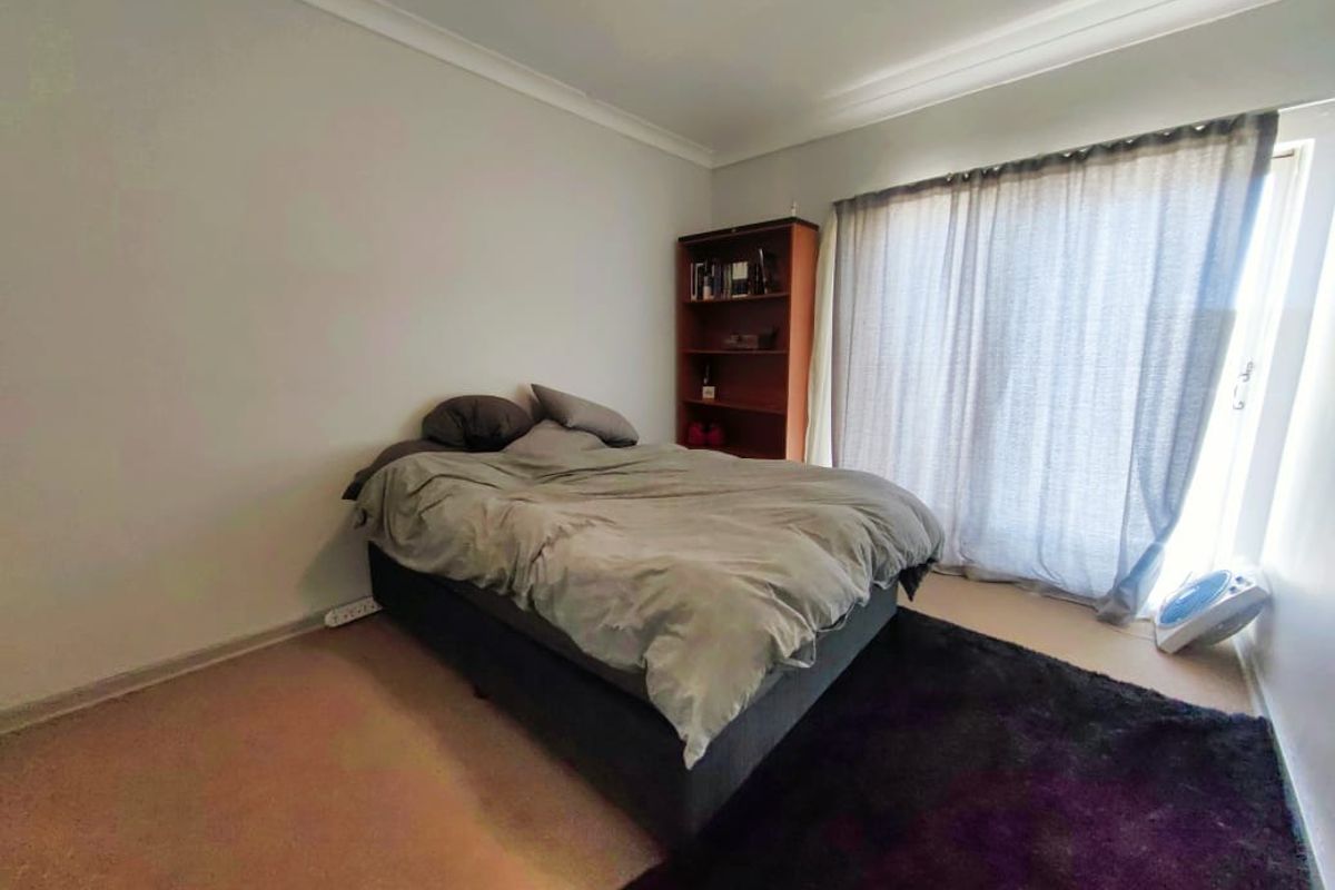 A bedroom featuring neutral walls, carpeted flooring, and a sliding door with curtains leading to an outdoor area.