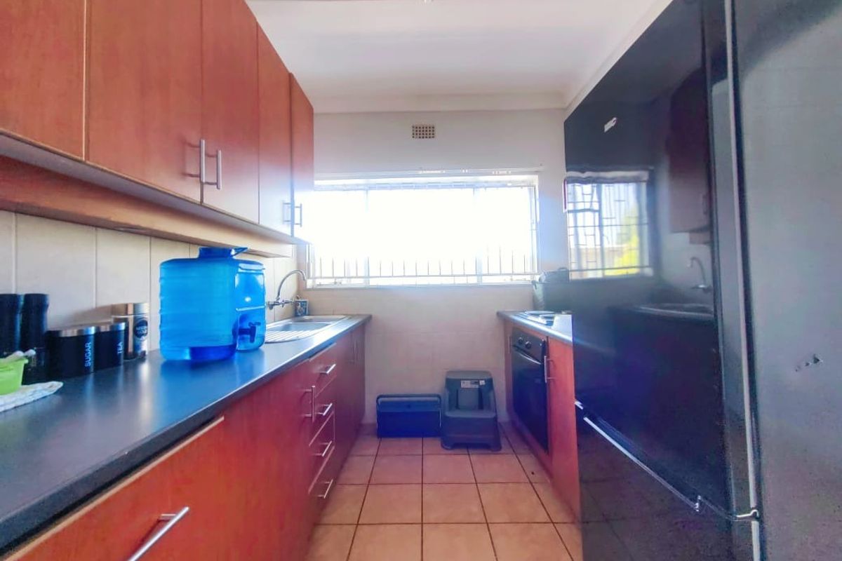 A functional galley-style kitchen featuring wood-finish cabinetry, tiled flooring, a built-in oven, and a window with security bars.