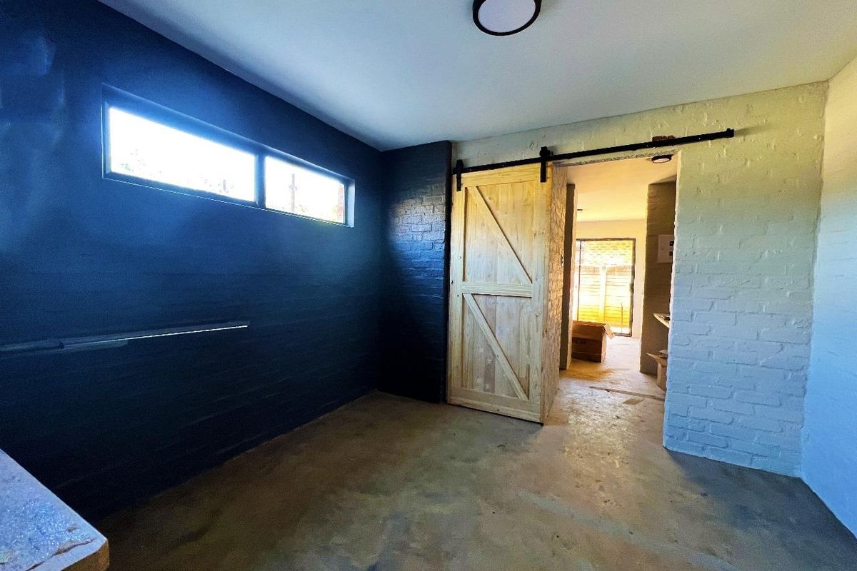An interior room featuring a sliding barn door, exposed brick walls, and a modern flush-mount ceiling light, currently in an unfinished state.