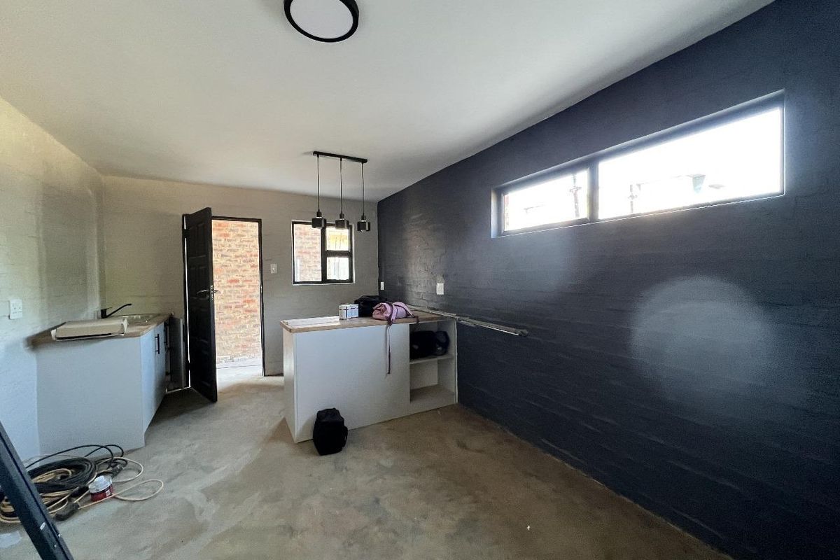 A functional kitchen area featuring a central island, built-in cabinetry, modern pendant lighting, and a striking dark accent wall with horizontal windows.