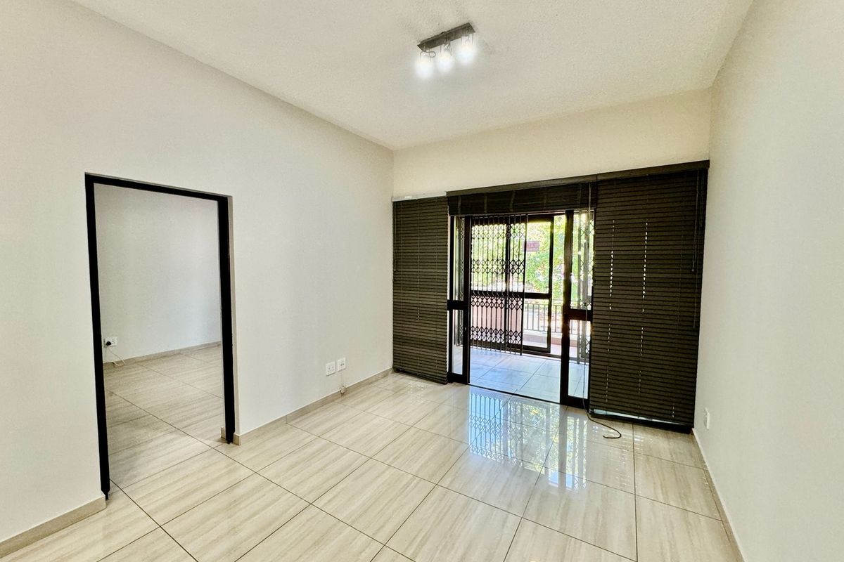 A bright, empty living area featuring neutral tiled flooring, modern ceiling lighting, and sliding glass doors leading to a private balcony.