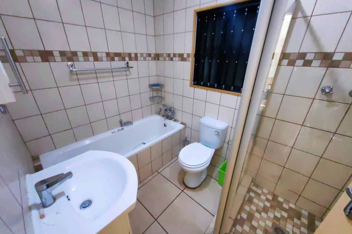 A functional bathroom featuring a bathtub, separate shower enclosure, pedestal basin, and toilet with tiled walls and flooring.