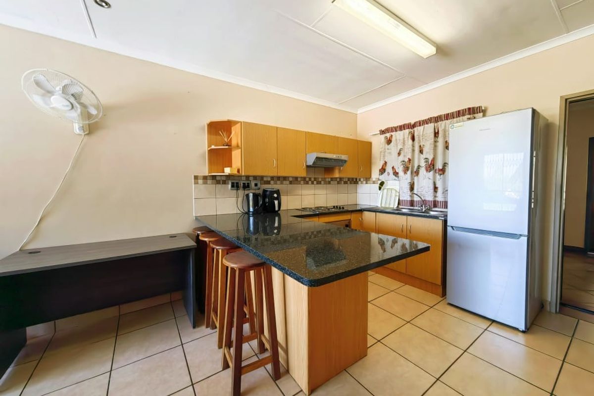 Functional kitchen featuring granite countertops, wooden cabinetry, a built-in hob, and tiled flooring, offering a practical layout for daily meal preparation.