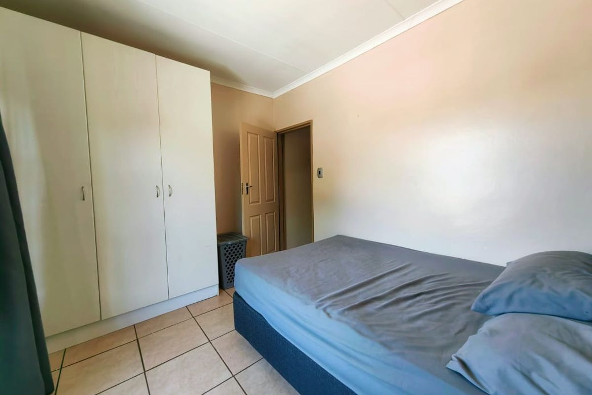 A functional bedroom featuring built-in cupboards, tiled flooring, and a neutral color palette, providing a practical living space.