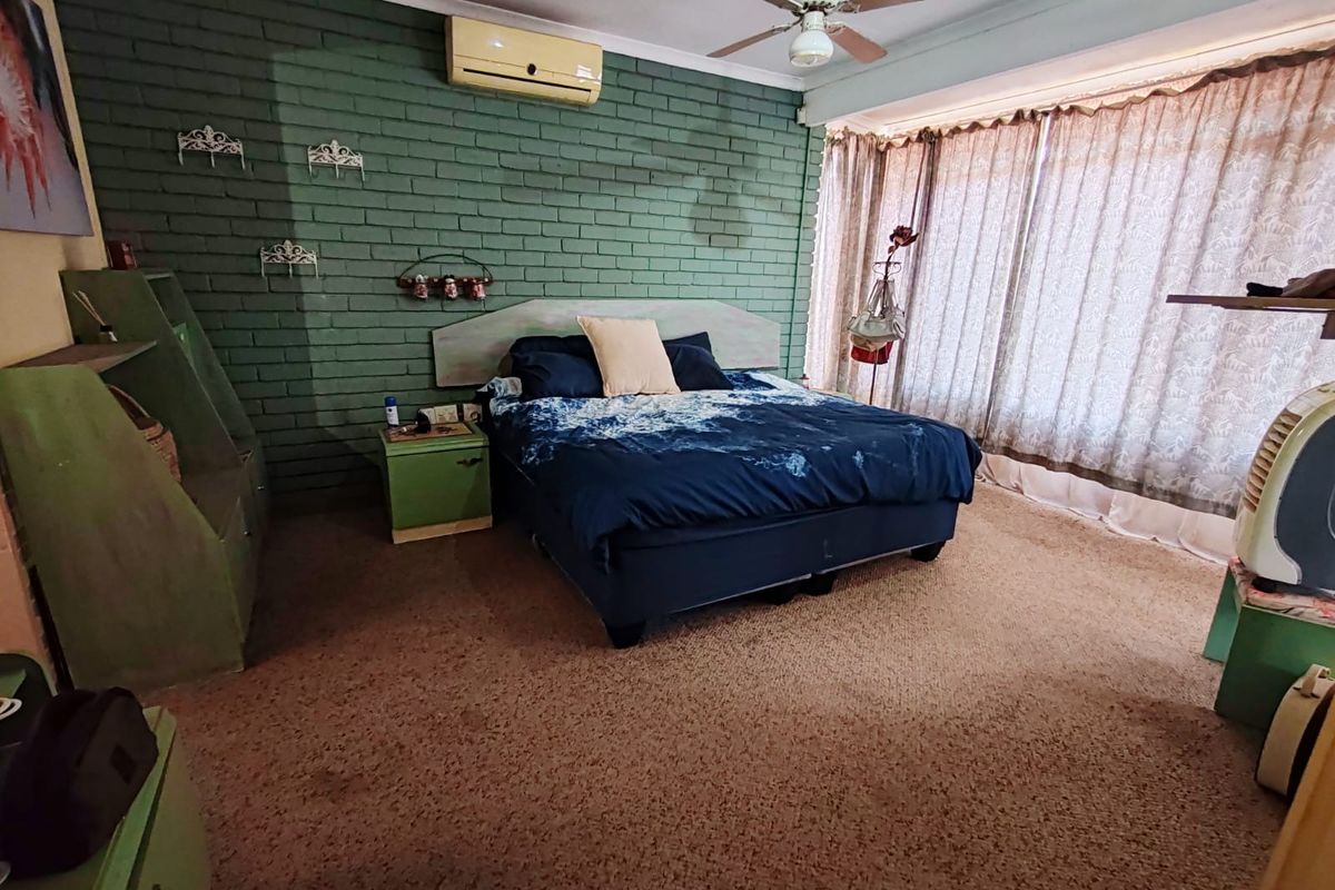 Spacious bedroom featuring a painted brick feature wall, ceiling fan, and wall-mounted air conditioning unit with large window coverage.